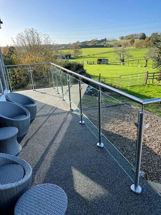A stainless steel and glass rail around a deck, looking out over fields