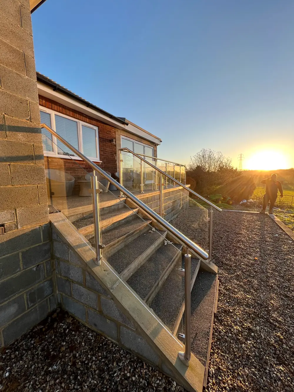 A stainless steel and glass rail beside outdoor steps, at sunset