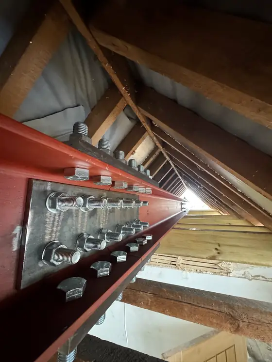 The bolted joint where one red steel beam meets another, under a roof