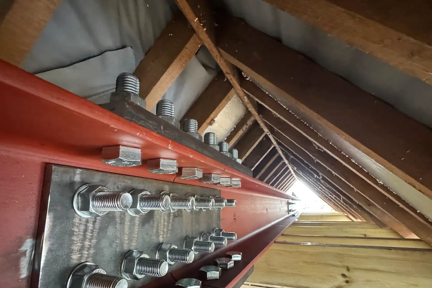 The bolted joint where one red steel beam meets another, under a roof