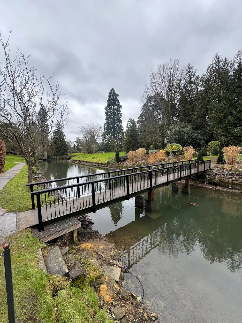 A steel footbridge across a lake in landscaped gardens