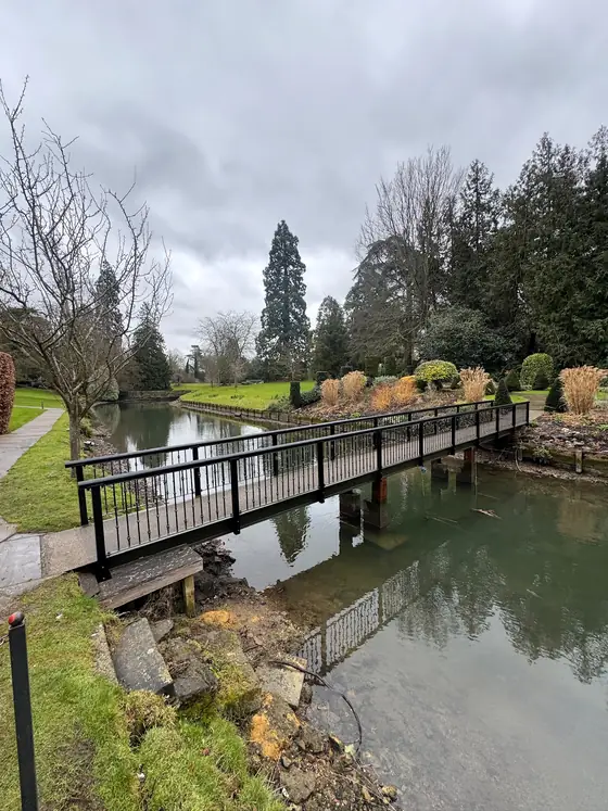 A steel footbridge across a lake in landscaped gardens