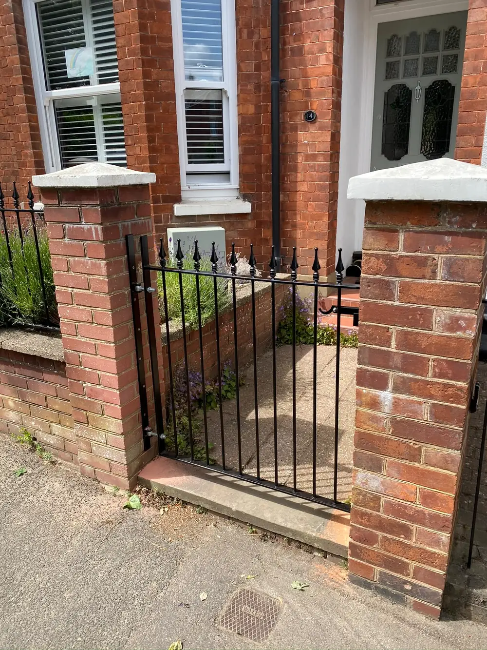 A black gate and railings between brick pillars at an old house