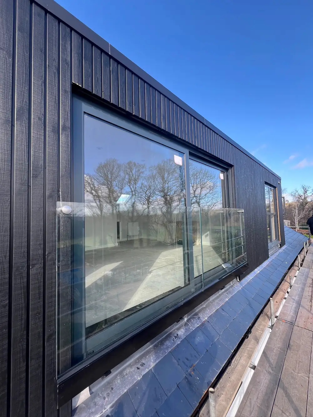 A glass panel with no frame around it across a first floor door, on a wall clad in dark timber boards