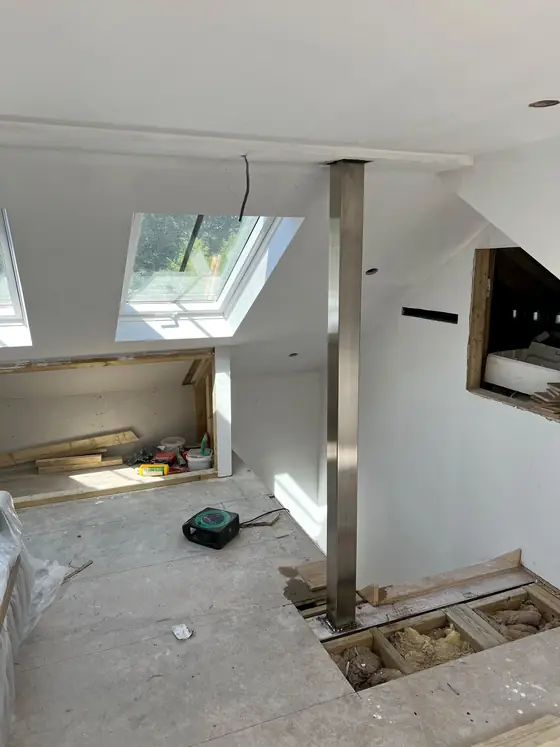 A loft part way through being converted, with a steel post standing floor to ceiling on a bare concrete floor