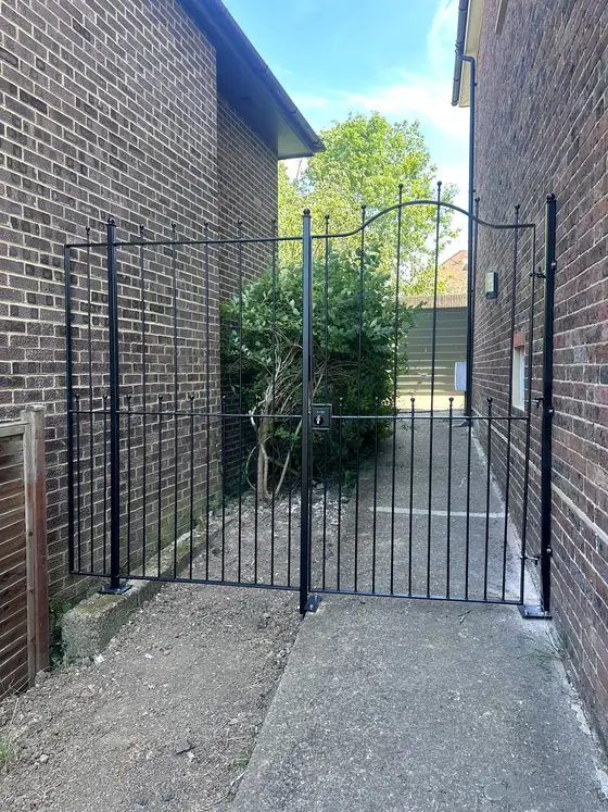 Ornate black gates closing a passage between two brick walls