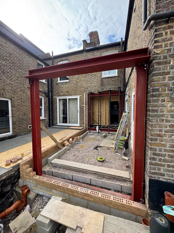 A red steel frame and beam over a new opening at the back of a house
