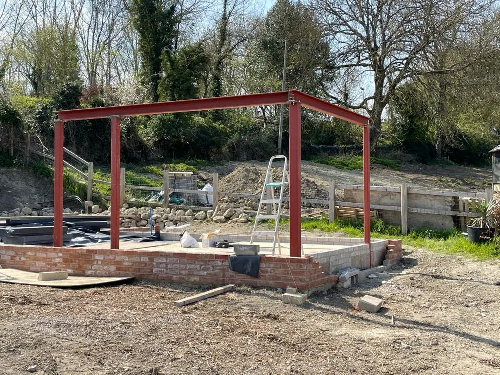 A red steel frame standing finished on its brick base, with open ground behind it