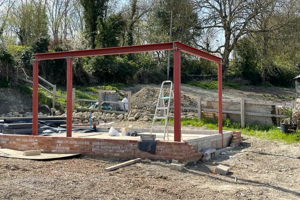 A red steel frame standing finished on its brick base, with open ground behind it