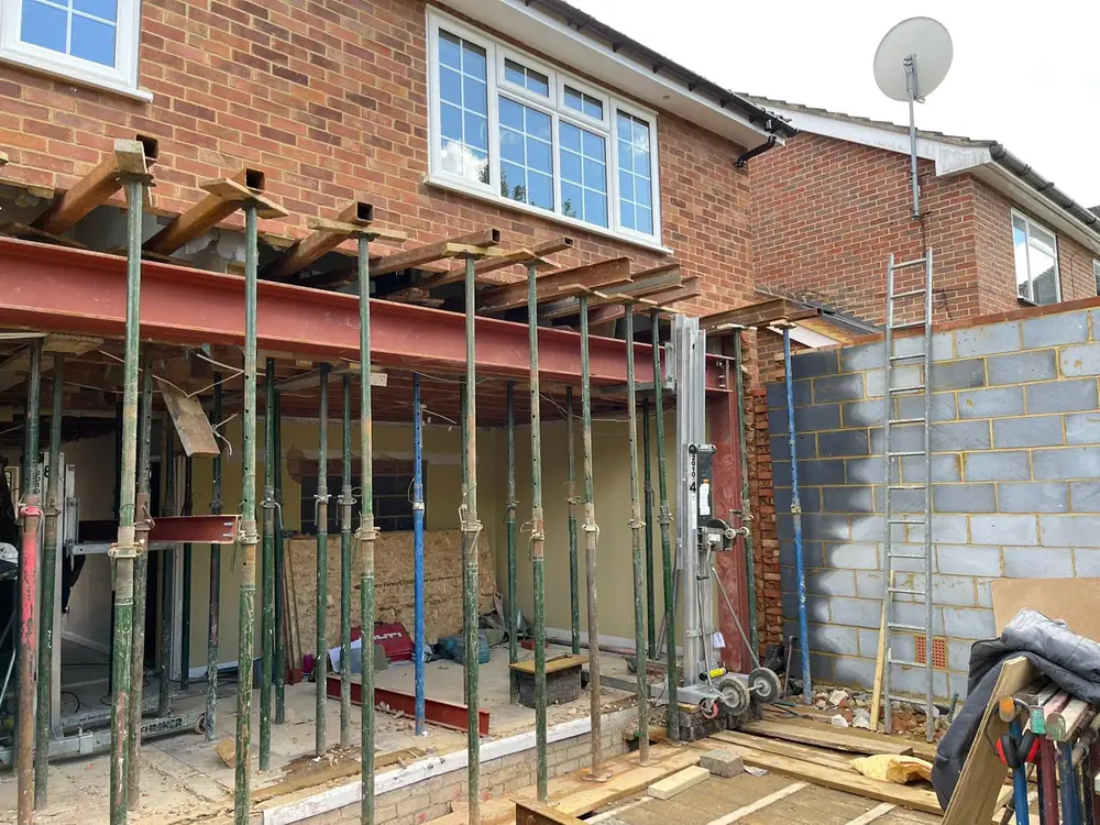 Adjustable steel legs and red beams holding the back of a house open part way through the work