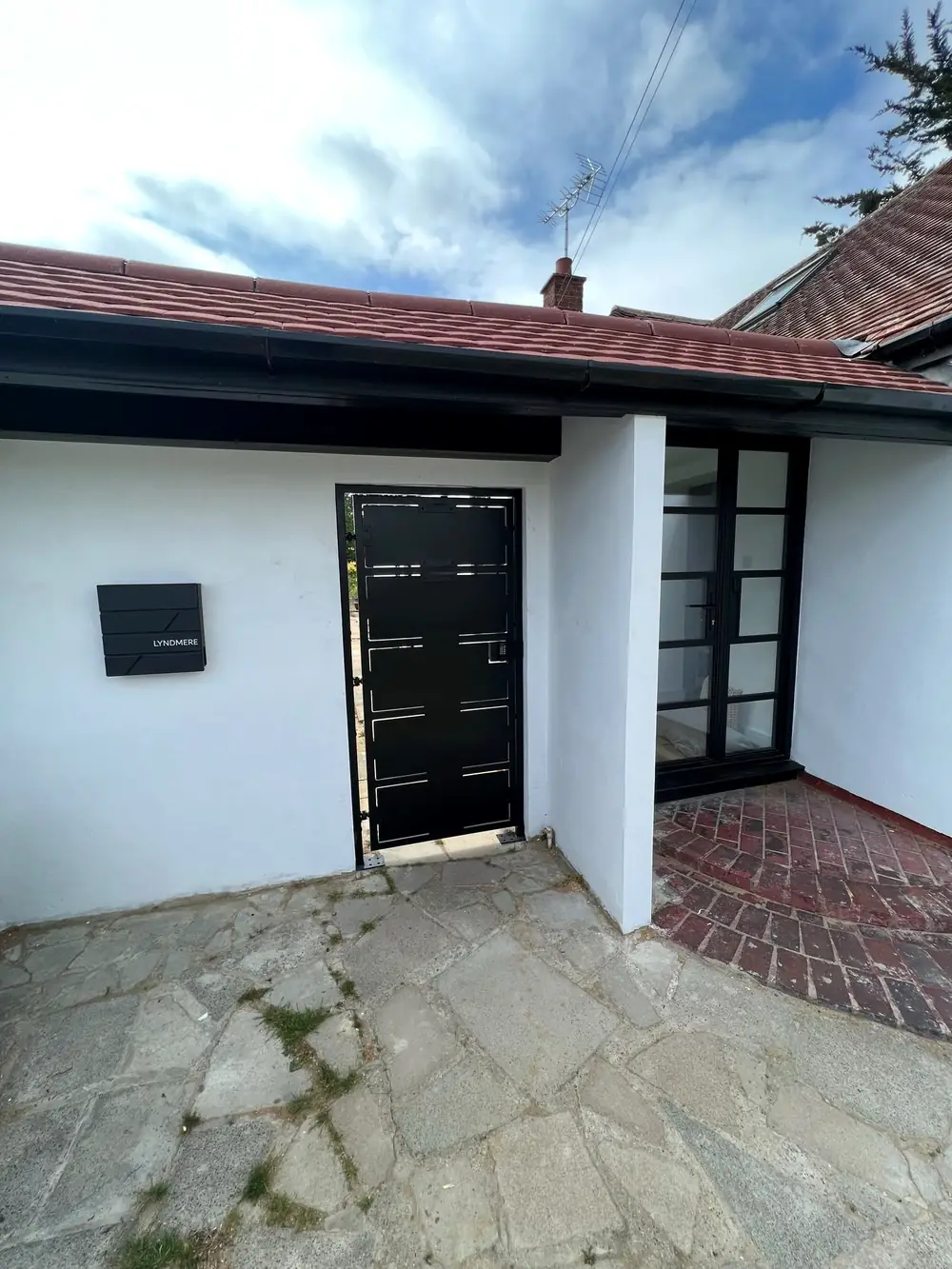 A black slatted steel door set in a smooth plastered wall