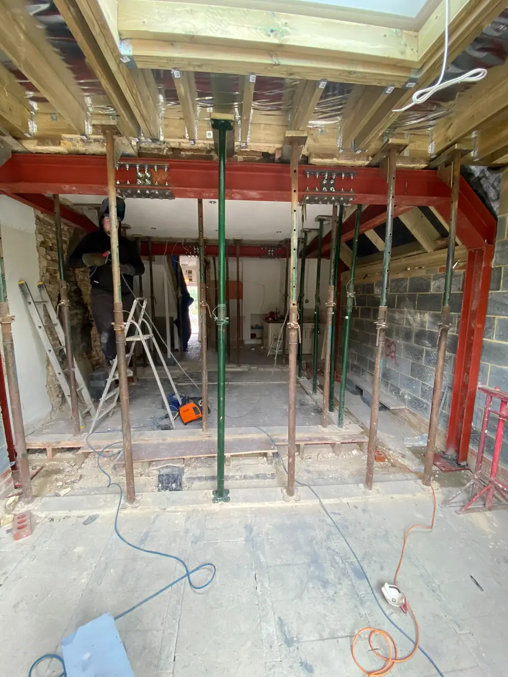 Red steel beams and adjustable legs inside a ground floor stripped back to bare walls