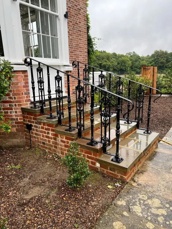 An ornate scrolled iron handrail and uprights on brick steps