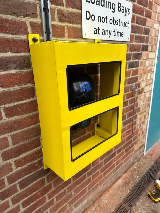 A yellow steel box bolted to a brick wall, made to fit